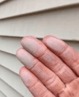 Close-up of hand showing chalky white oxidation residue on vinyl siding
